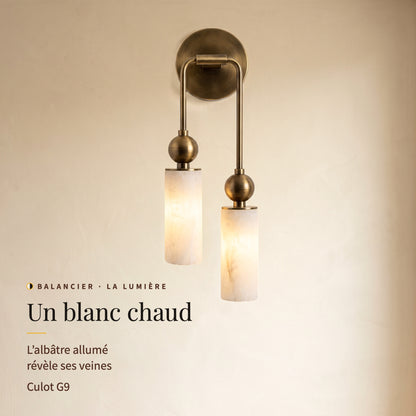 Balancier, applique allumée vue de face : lumière blanc chaud à travers l’albâtre veiné, culot G9
