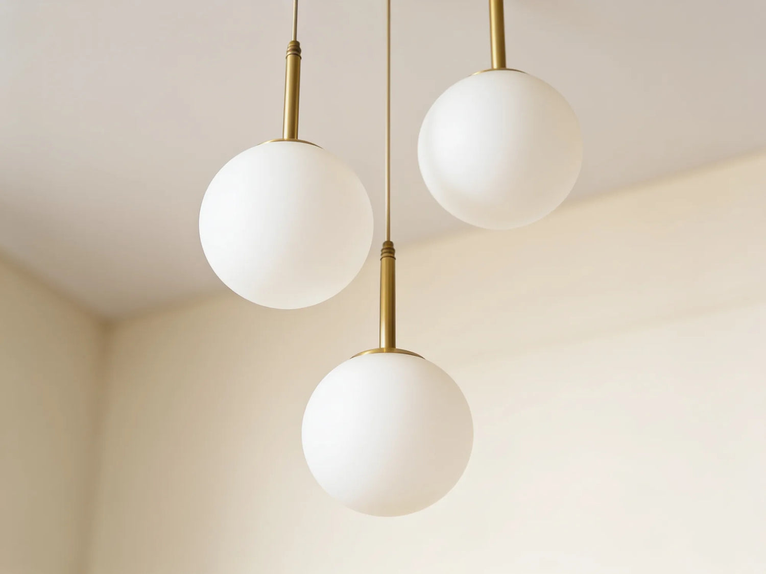 Gros plan sur les trois globes en verre opalin étagés à trois hauteurs, sur leurs tiges en laiton brossé